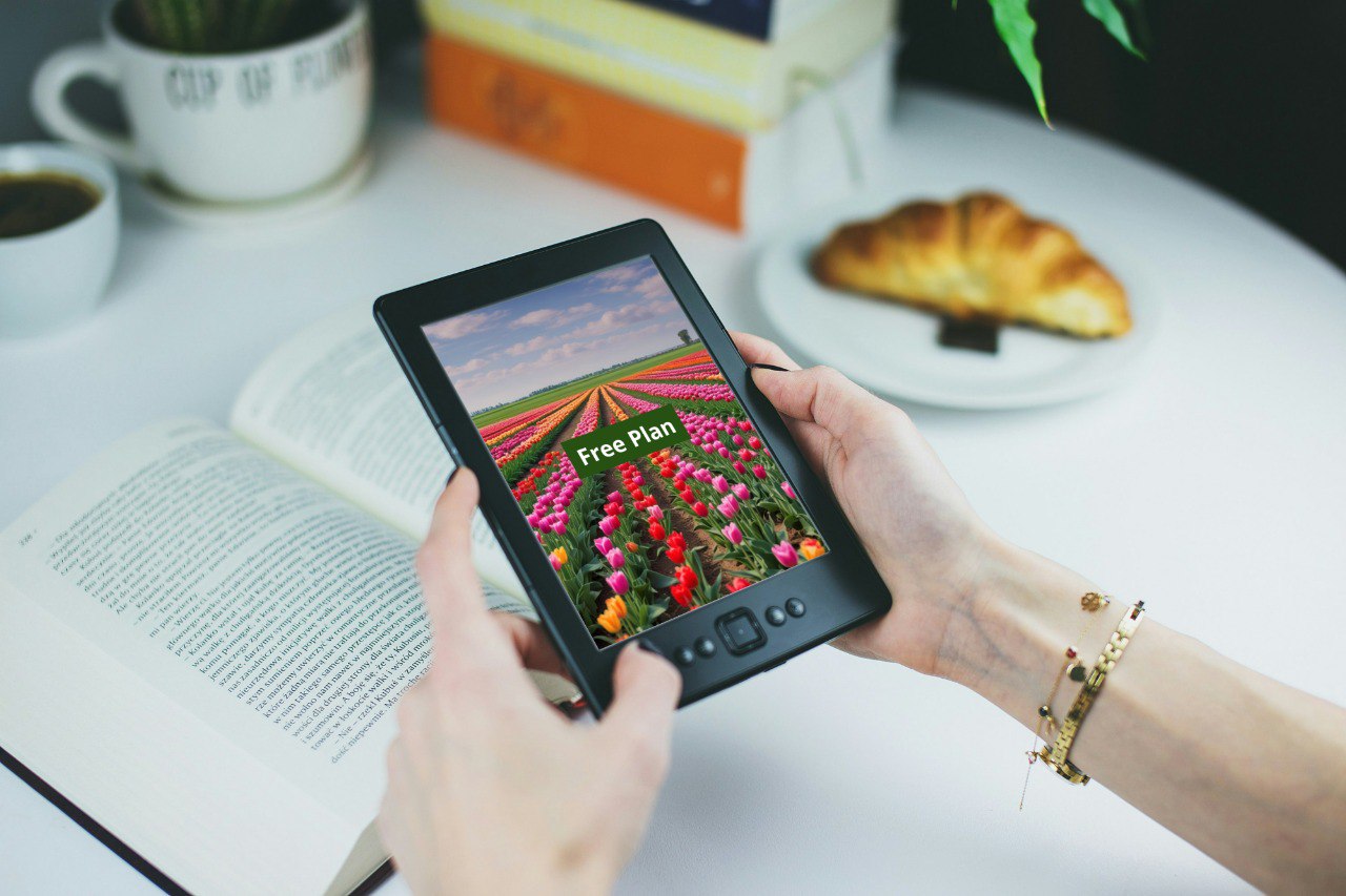 Person holding a digital tablet with a C++ course 'Free Plan' on a table with books and a croissant.