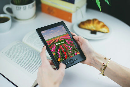Person holding a digital tablet with a C++ course 'Free Plan' on a table with books and a croissant.