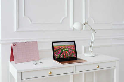 Laptop displaying 'Logic Flow' C++ course on a white desk with a calendar and lamp in a minimalistic room.